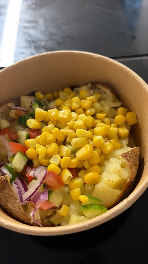 A kraft bowl of jacket potato topped with sweetcorn, tomato, pepper and red onion salad