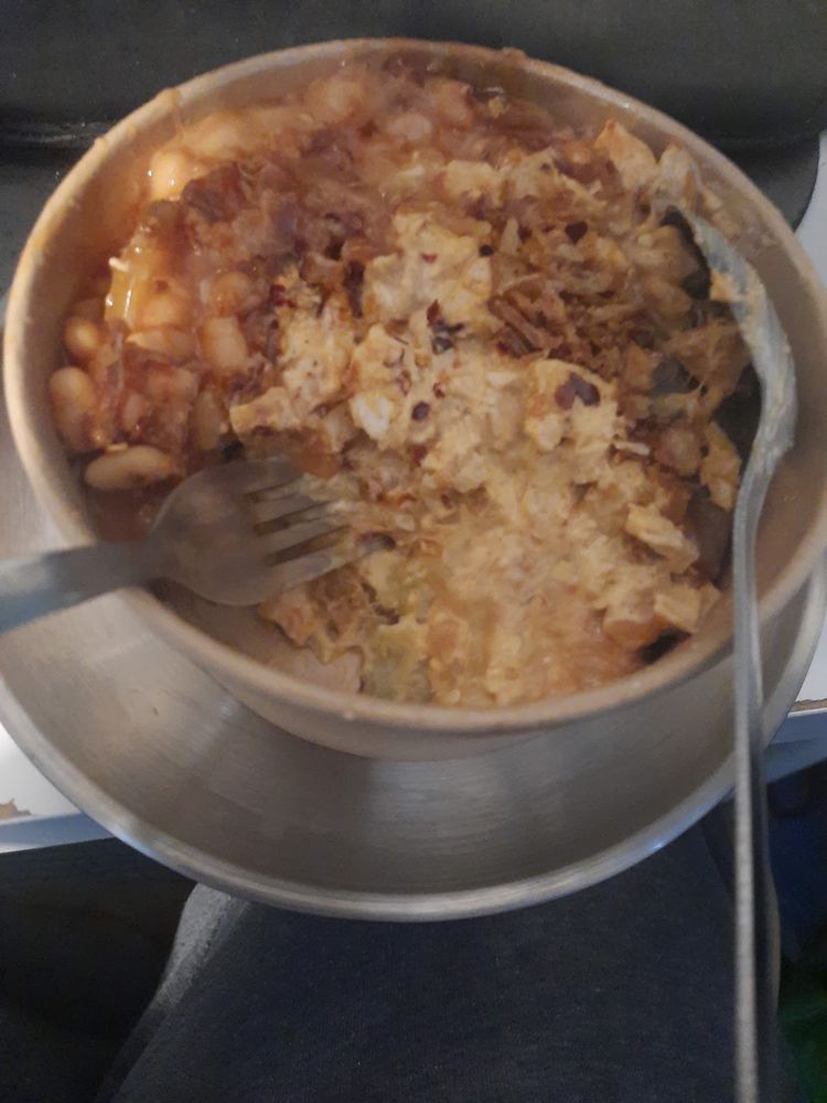 A bowl of jacket potato with baked beans and melted cheese, a metal fork resting in it